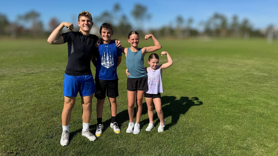Four children smiling and flexing together in a sunny field
